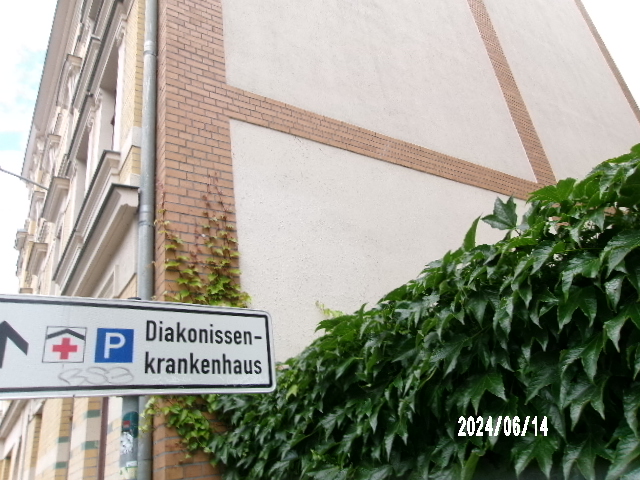Wegweiser zum Diakonissenkrankenhaus neben begrüntem Gebäude an einer Ecke.